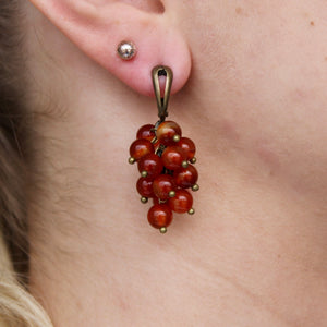 Collection of brown-red Carnelian stone orb dangle earrings with gold clasps.